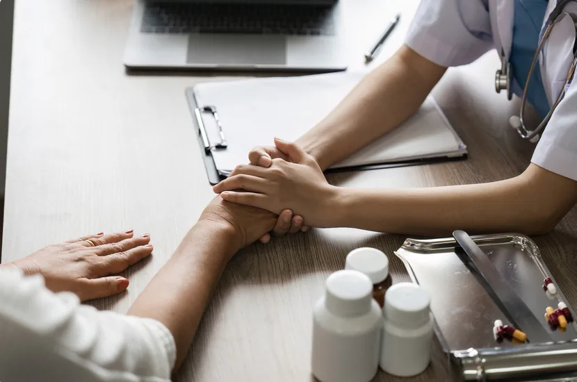 Un cadru medical ține mâna unui pacient în timpul unei consultații.